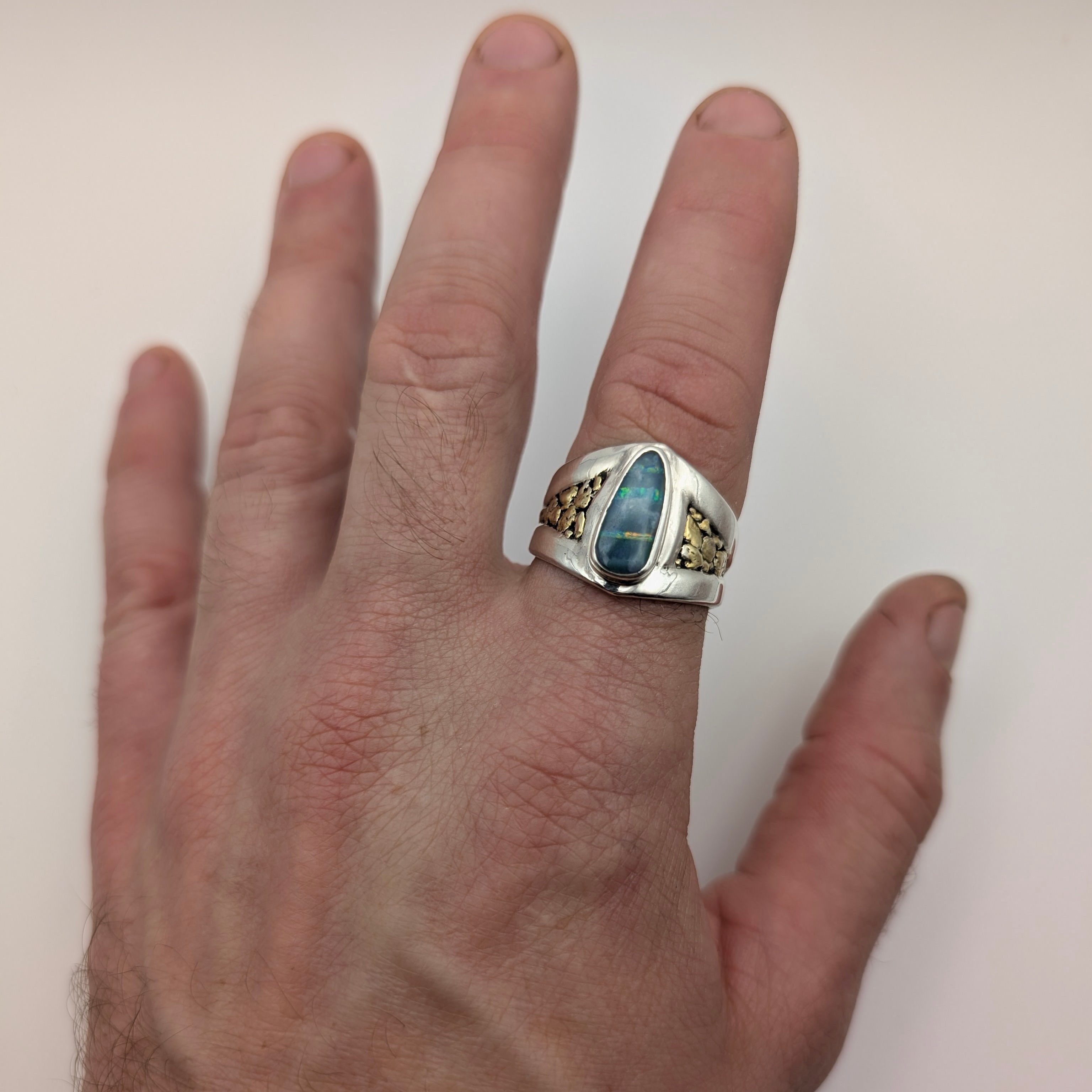 Hand wearing a silver ring with a blue stone on a plain background