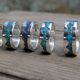 Silver rings with blue and green inlay on a wooden surface