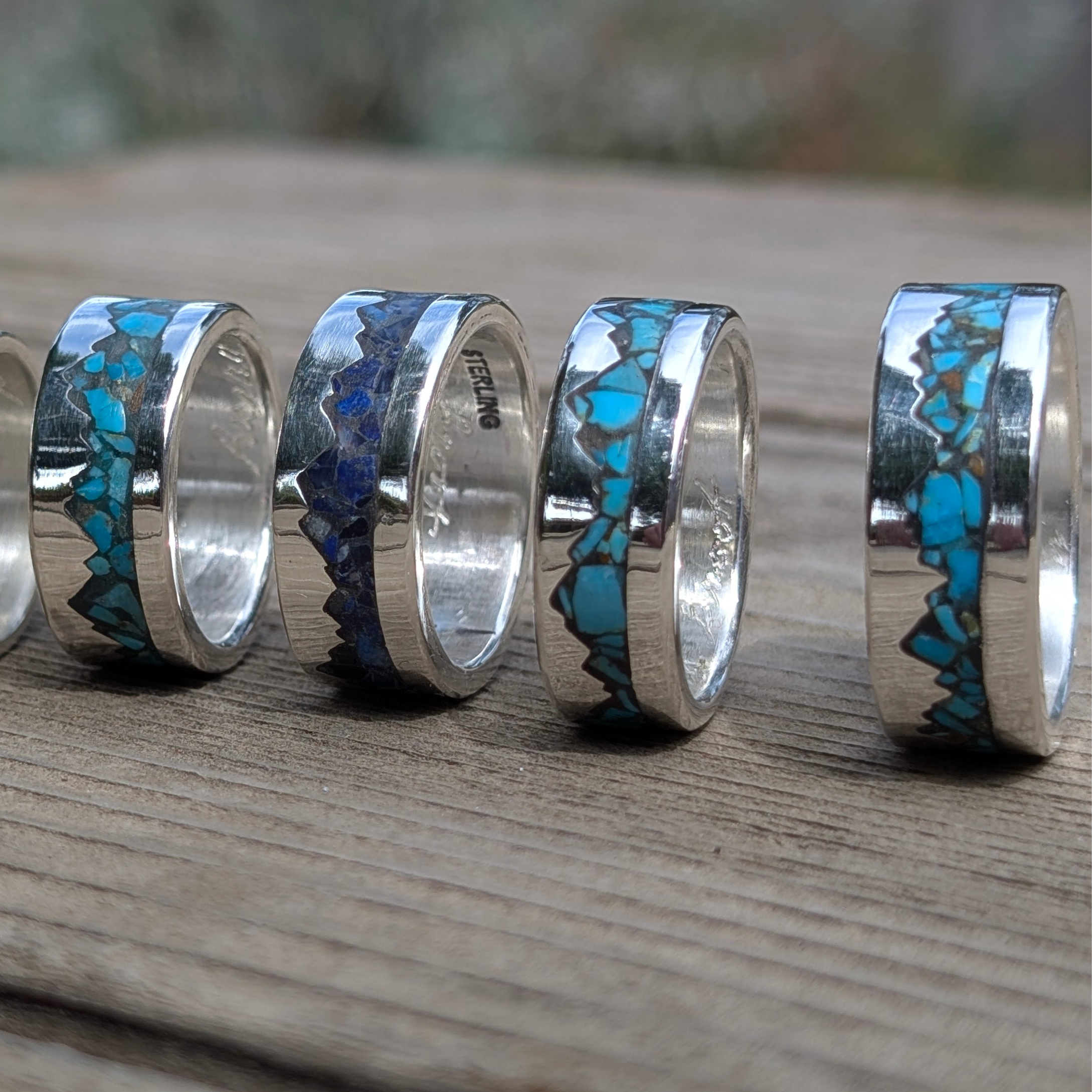 Silver rings with blue and green inlay on a wooden surface