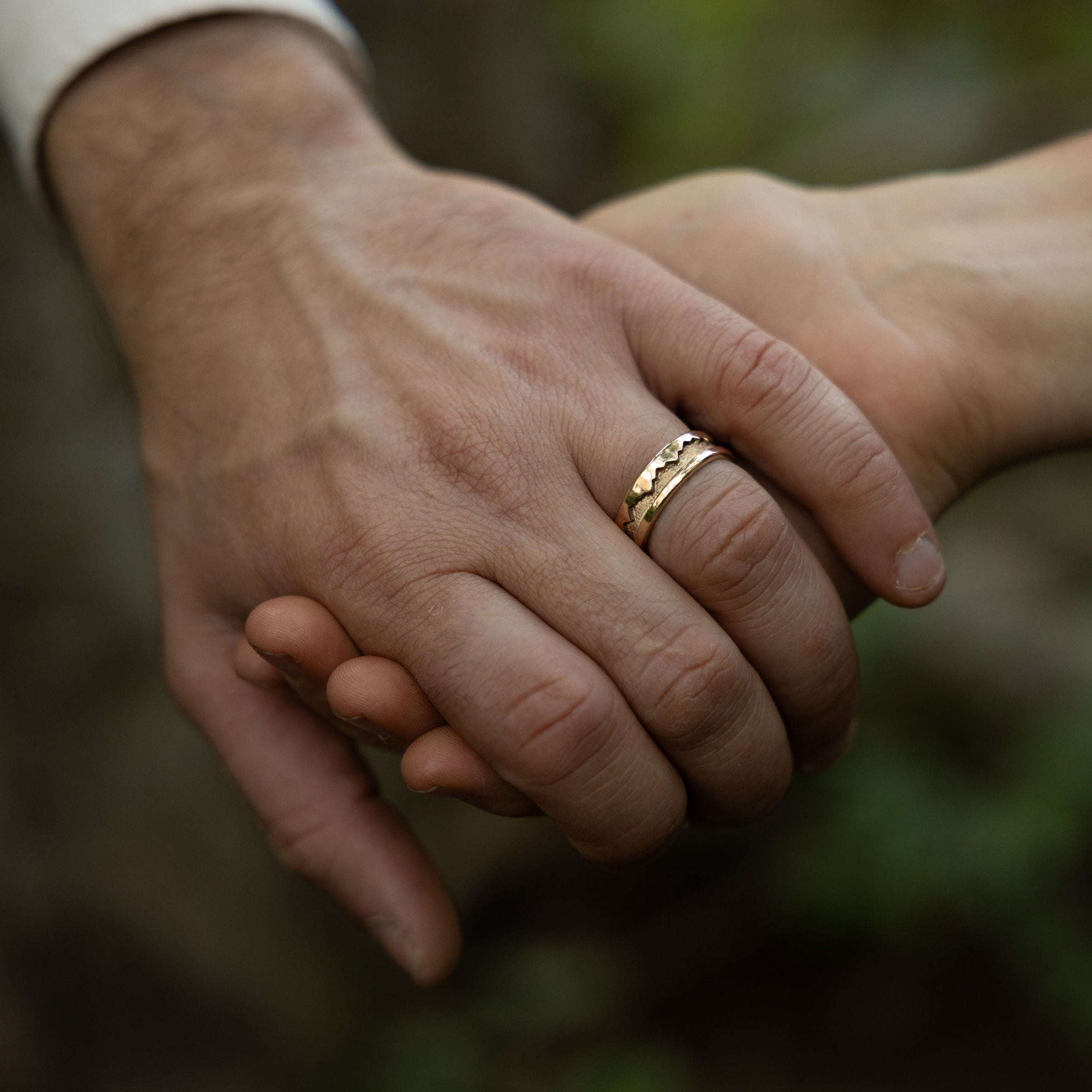 Two hands holding each other with a blurred natural background