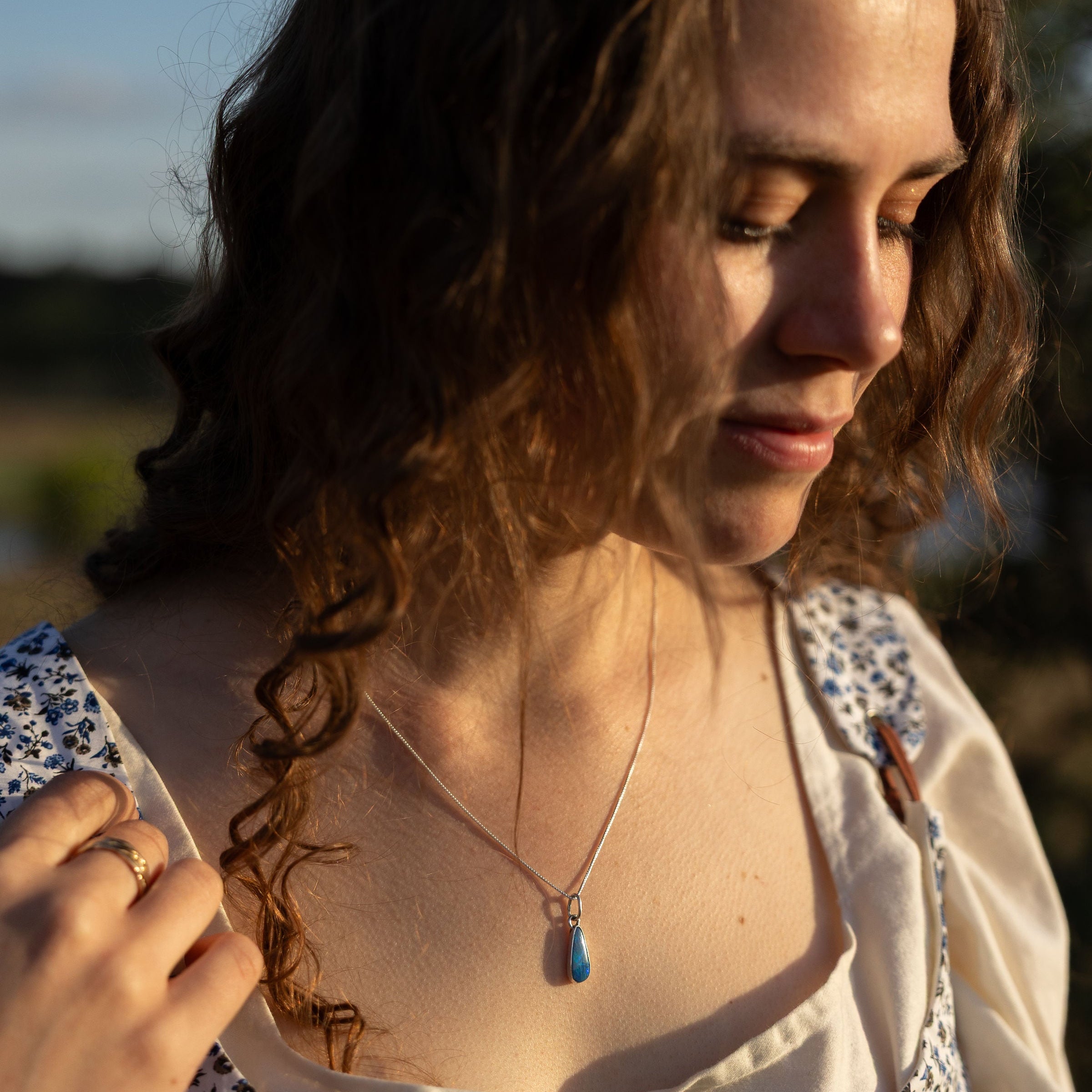 Woman with long brown hair looking down, wearing a patterned top and necklace.