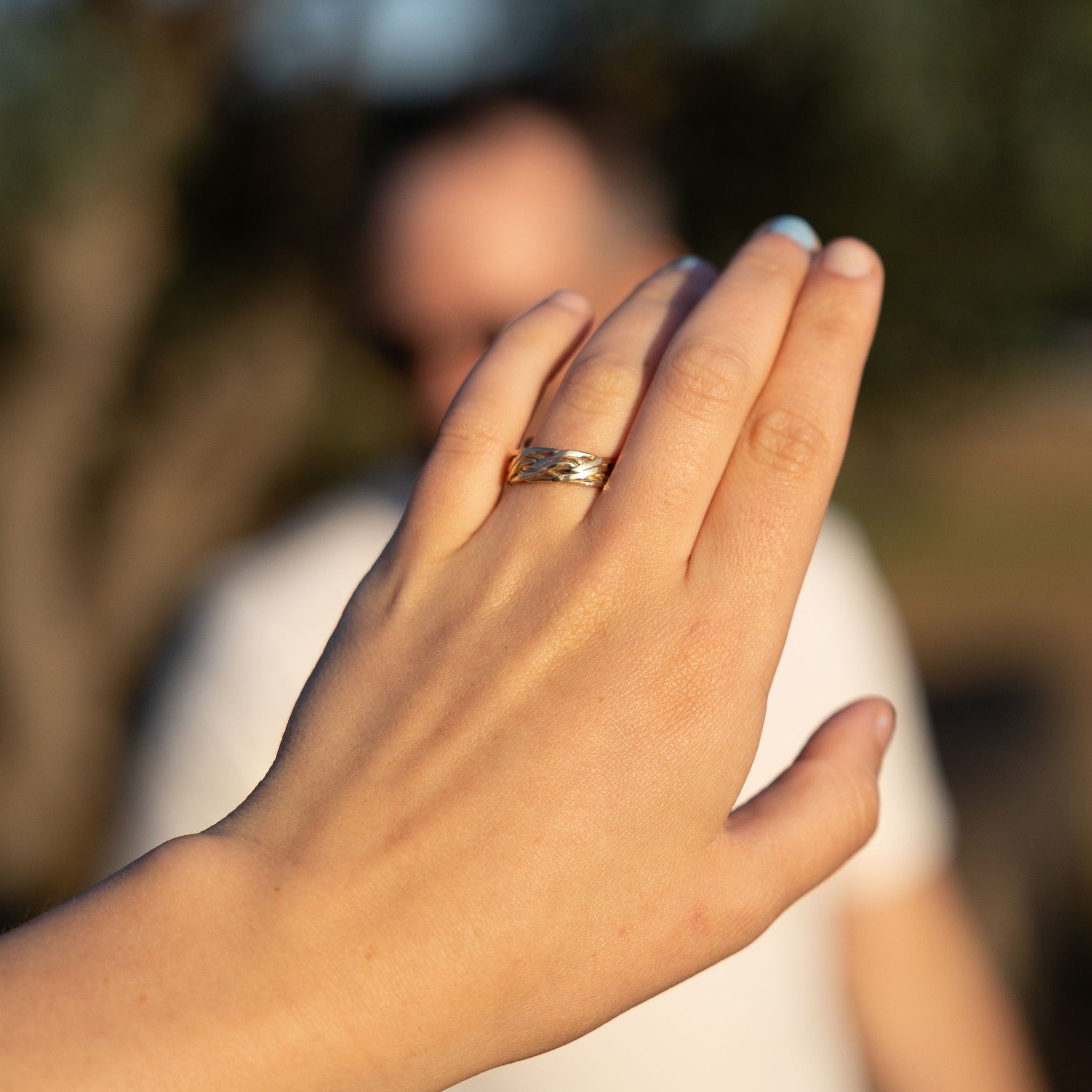 Hand with a ring held up against a blurred natural background