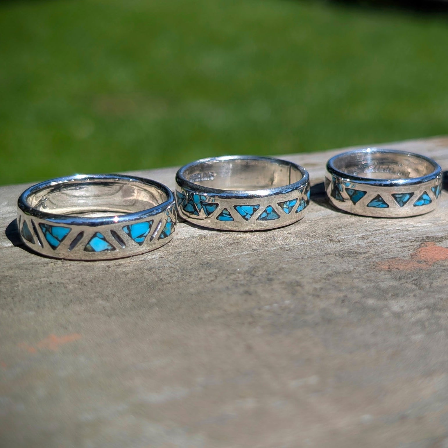 Four silver rings with blue gemstone inlay on a stone surface with a blurred green background
