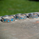 Four silver rings with blue gemstone inlay on a stone surface with a blurred green background