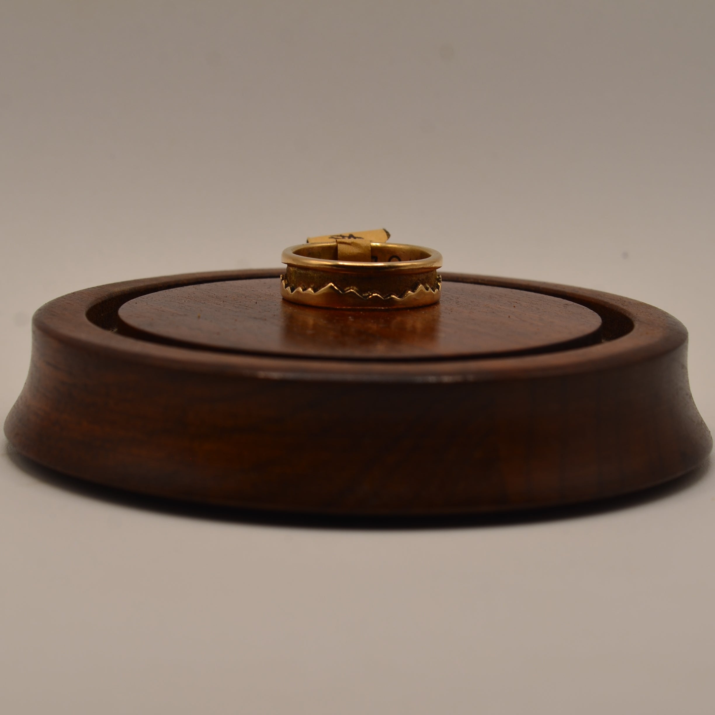Gold ring on a wooden display stand against a plain background