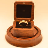 Wooden ring box with a ring inside on a matching wooden stand.