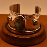 Silver bracelet with a central turquoise stone on a wooden stand against a brown background