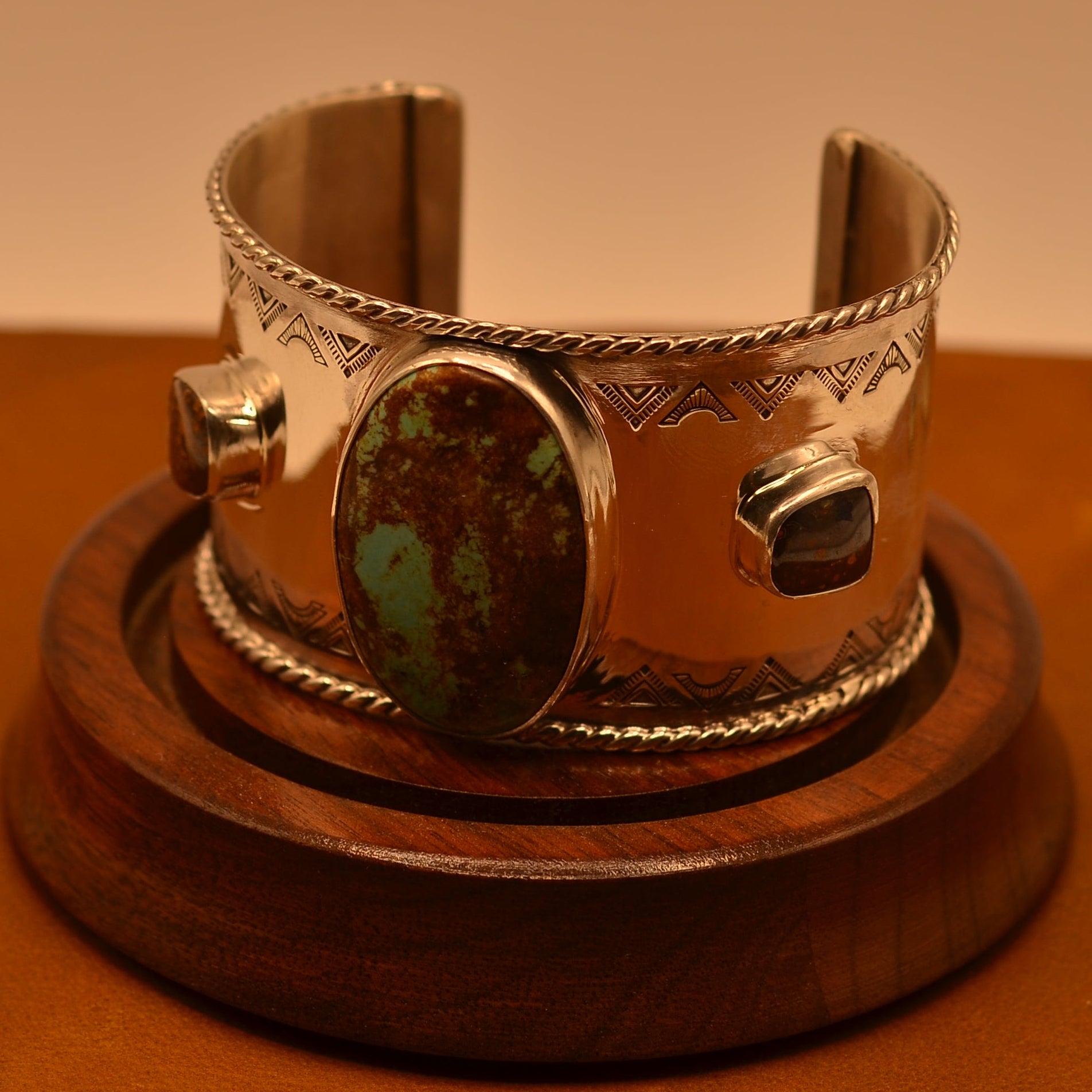 Silver bracelet with a central turquoise stone on a wooden stand against a brown background