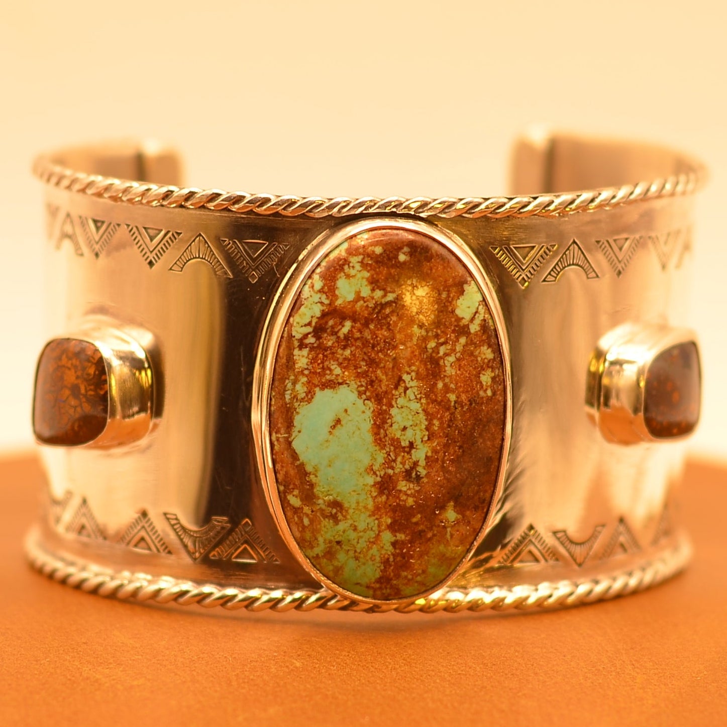 Silver bracelet with a central turquoise stone framed by boulder opals on an leather surface