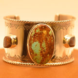 Silver bracelet with a central turquoise stone framed by boulder opals on an leather surface