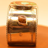 Silver cuff with intricate design on a leather surface