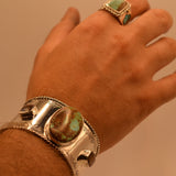Hand wearing a silver bracelet with turquoise stones against a beige background