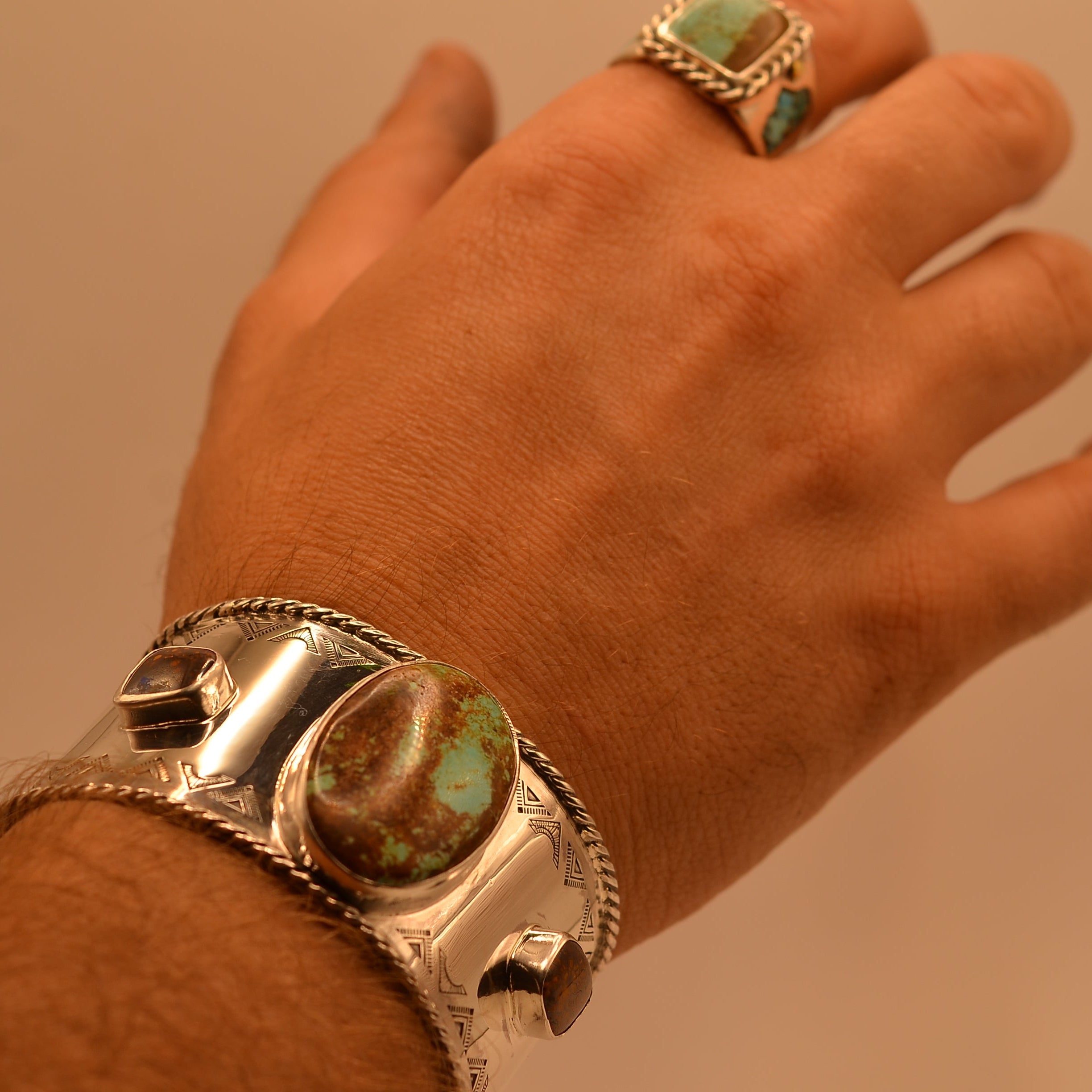 Hand wearing a silver bracelet with turquoise stones against a beige background
