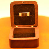 Wooden ring box with a gold ring inside on a yellow background