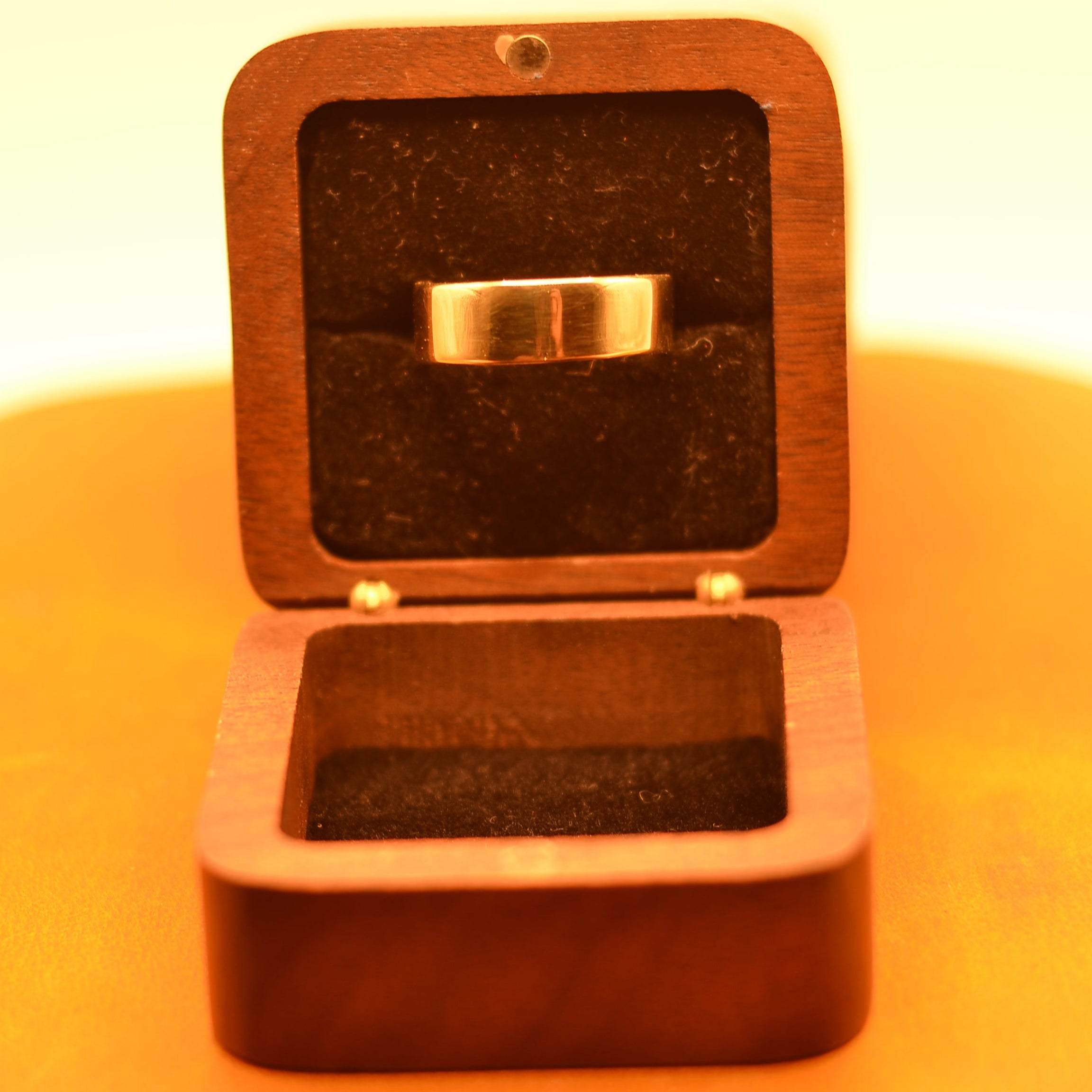 Wooden ring box with a gold ring inside on a yellow background