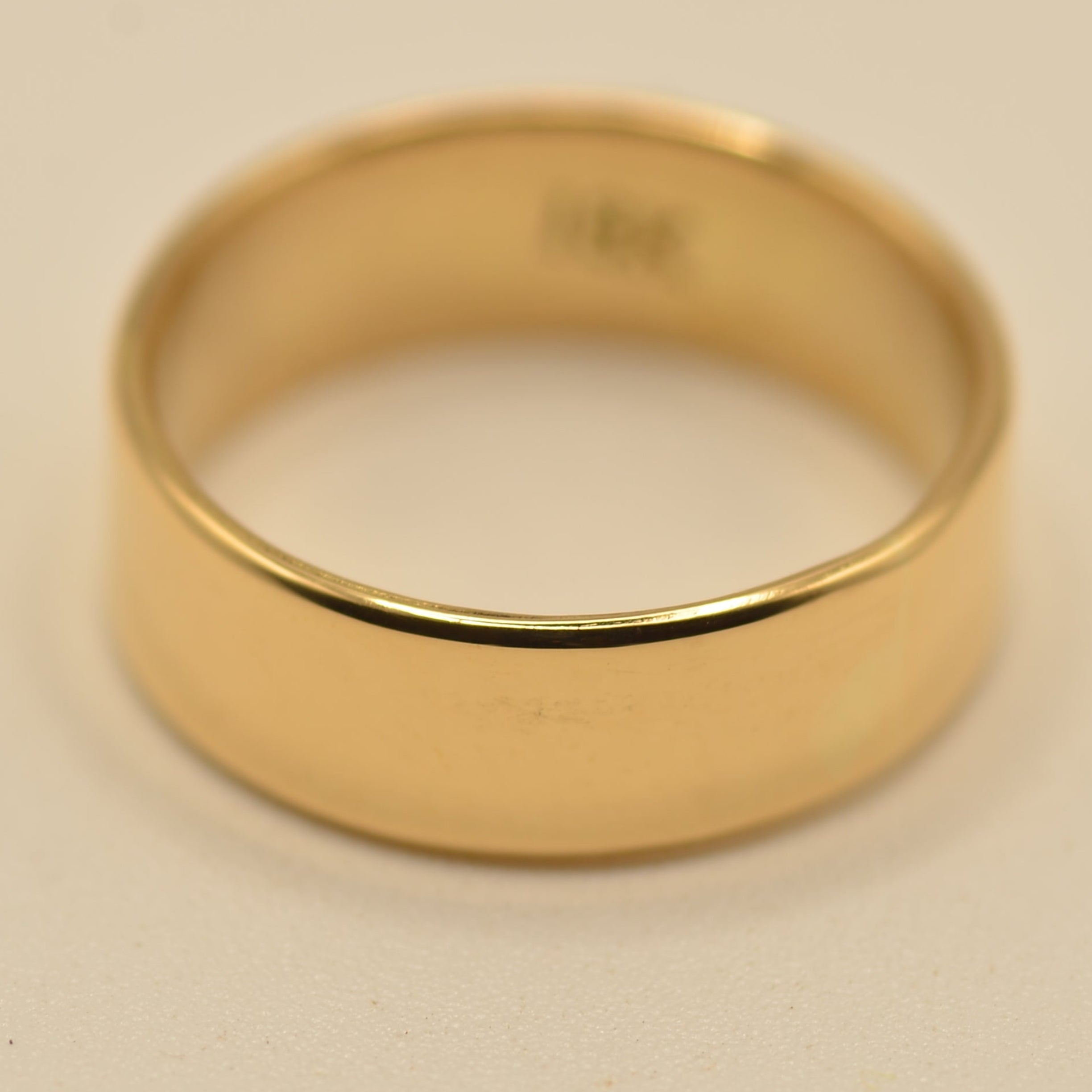 A classic yellow gold band ring with a smooth, polished finish, photographed on a plain light beige background.