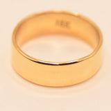 A simple yellow gold band ring with a flat, polished surface, photographed on a plain off-white background.