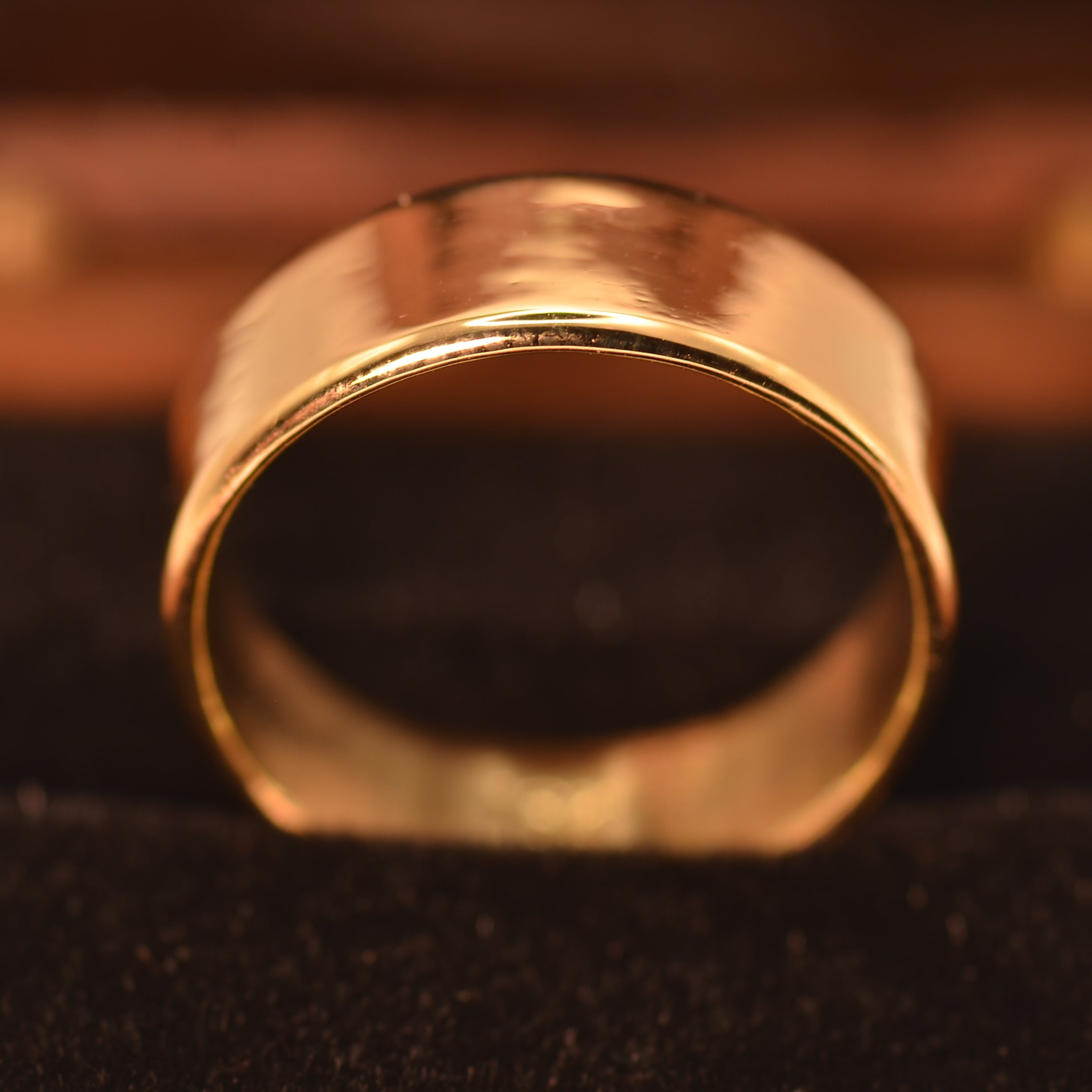 A wide, polished yellow gold band ring displayed on a black velvet ring cushion inside a wooden box.
