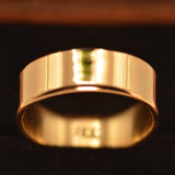 A polished yellow gold band ring displayed in a black velvet jewelry box.