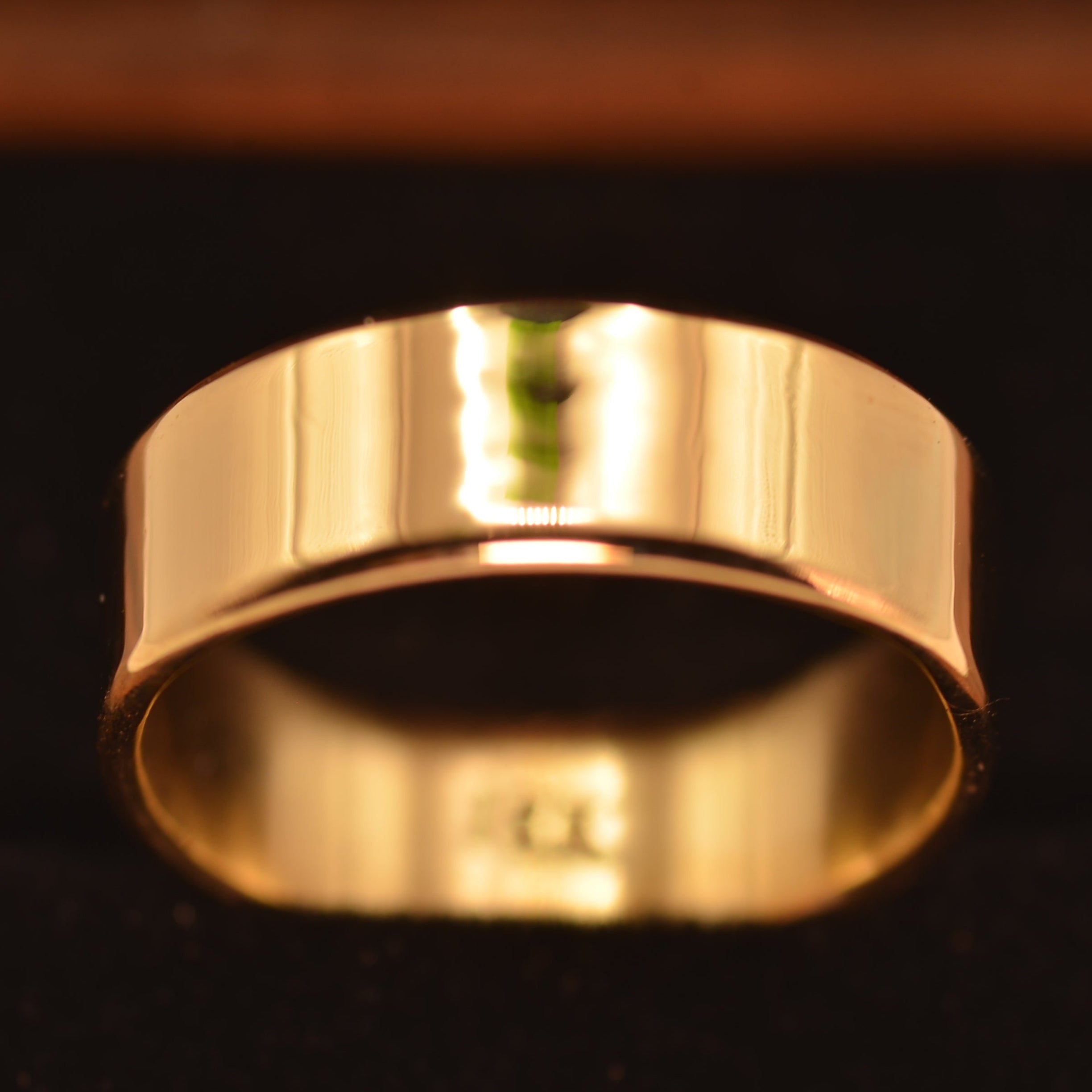 A polished yellow gold band ring displayed in a black velvet jewelry box.