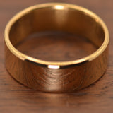 A polished gold band ring with a resting on a dark brown wooden surface.