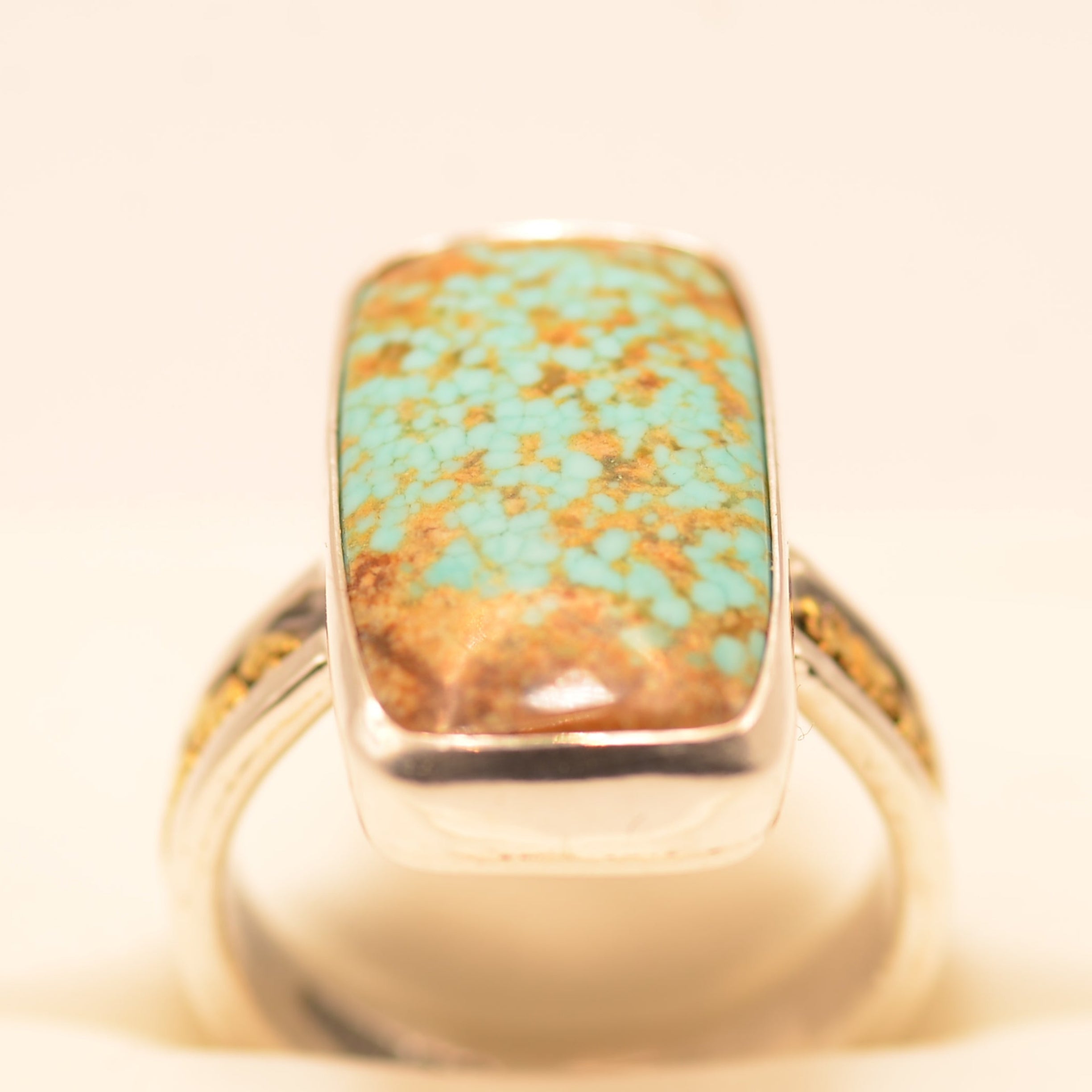 A sterling silver ring featuring a large, rectangular turquoise stone with prominent golden-brown matrix, displayed on a cream-colored ring stand.