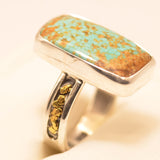 A sterling silver ring featuring a rectangular turquoise stone with prominent coppery brown matrix, displayed on a soft cream-colored surface.