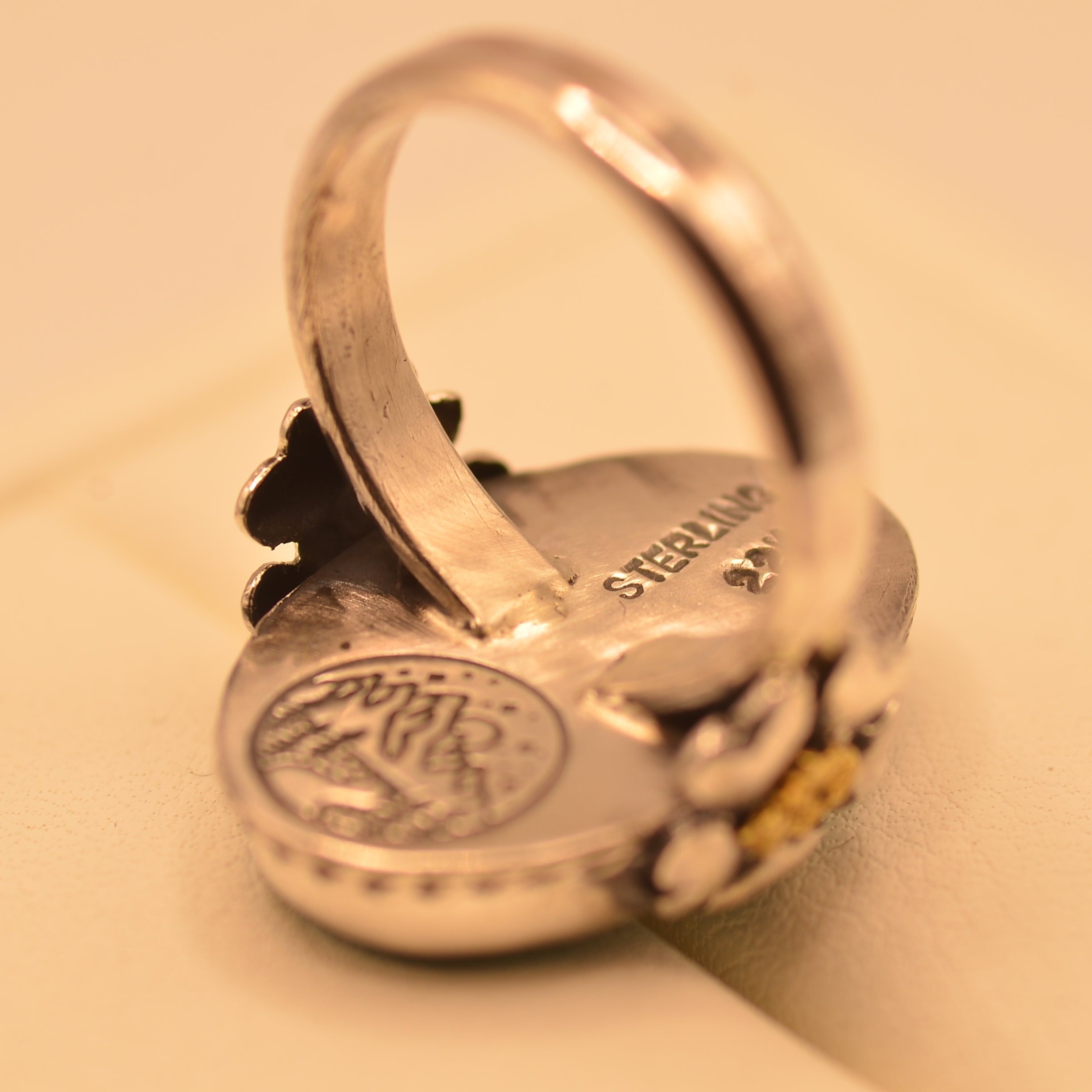 A sterling silver ring with a circular medallion face and small yellow gemstone accents, resting on a beige surface.