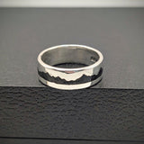 Silver ring with a textured design on a black surface
