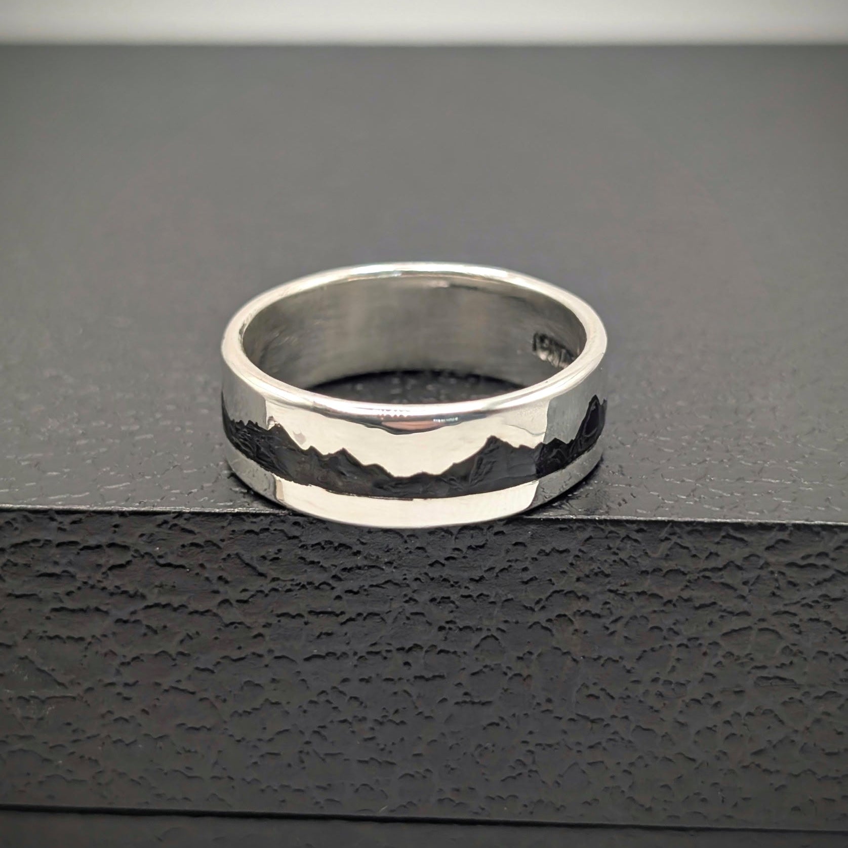 Silver ring with a textured design on a black surface